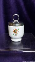 First egg coddler showing white porcelain with orange and red floral pattern and silver metal lid with loop handle.