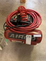 Front view of red Airco air compressor with coiled red hose and black air tool placed on top.