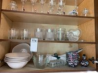 Wide view of cabinet shelf with crystal drinking glasses, white and clear bowls, small floral porcelain decorative bowls and vase.