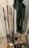 View of multiple fishing rods, fishing reels on wooden racks, and green fishing waders hanging