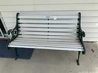 Front view of outdoor garden bench with white wooden slats and dark green decorative cast iron armrests and legs.