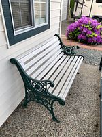 View of the full garden bench showing white wooden slats and green cast iron sides with floral design.