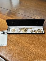 Photo showing the full set of assorted gold-tone jewelry pieces inside a black case on a wooden surface.