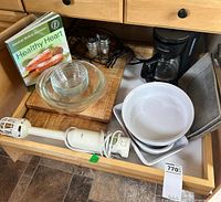 Kitchen drawer containing hand mixer, coffee maker, glass bowls, white casserole dishes, wooden cutting board, salt & pepper shakers.