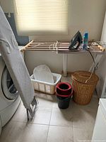 Photo showing laundry essentials including iron, ironing board, drying rack, hampers, and mop bucket arranged in a laundry room corner.
