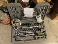 Overhead view of socket wrench set with various sizes of sockets, ratchet handles, and screwdriver attachment in gray plastic case, also a tape measure included
