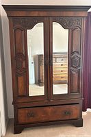 Front view of closed armoire cabinet showing two mirrored doors and ornate carved wood details.
