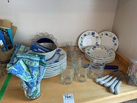 Overview of the blue themed dishware set including plates, bowls, glasses, knives, napkins, and artwork on a wooden surface.