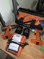 Photo showing two Ridgid cordless drills, two rechargeable batteries, a Ridgid Rapid Max battery charger, and a Ridgid branded carrying bag on a workbench.