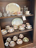 Full display of teacups, saucers, candle holders, and serving plates arranged in wooden cabinet shelves.