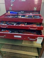 Image showing red metal toolbox with three open drawers filled with assorted hand tools.