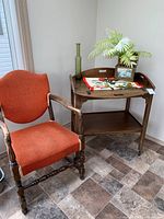 Photo showing burnt orange upholstered wooden armchair next to wooden tea cart with decorative items on top