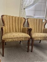 Two vintage chairs with gold upholstery and wooden accents shown side-by-side in room with carpet and window blinds.