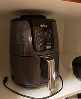 Black Ninja air fryer with handle and digital control panel, showing cooking settings on side and basket compartment open in one image