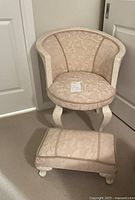 Front view of the beige upholstered barrel-back chair with matching footstool.