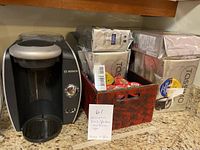 Bosch Tassimo coffee maker with multiple new packages of Tassimo coffee pods in a wooden holder on a kitchen counter.