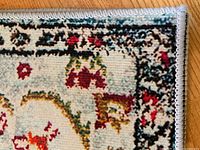 Close up of a multicolored rug with floral pattern and border stitching on wooden floor