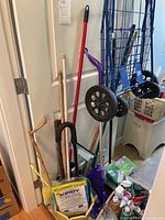 Full view of metal shopping cart, walking canes, broom handles, cleaning pads, manual vacuum, and other cleaning supplies