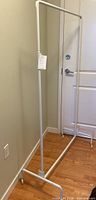 Clothing rack standing upright showing the full frame against a wall and door.