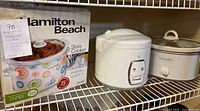Wide view of the two slow cookers and rice cooker on shelf, boxed Hamilton Beach crockpot on left