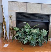 Two lacquered giraffe figurines next to a fireplace with the silk plant in front