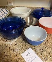 Blue glass covered casserole dish, six mixing bowls of various colors and sizes, two small stainless steel bowls on kitchen counter.