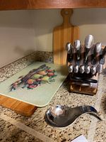 Wooden and glass cutting boards next to Sabatier branded wooden knife block holding knives and metal kitchen utensil on countertop.