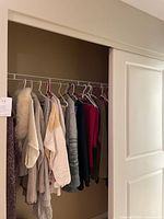 Closet with multiple knit sweaters hanging on white wire rack within a closet with beige walls and sliding door.