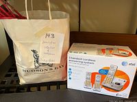 Photo of the white Hudson's Bay bag with label stating 'Collection of telephones' next to a boxed AT&T 3 handset cordless answering system.