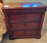 Front view of the wooden night table showing three drawers and round metal knobs.