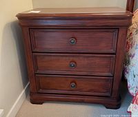 Front view of dark wooden night table with three drawers and round black knobs