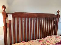Close-up front view of wooden headboard with vertical slats and rounded finials on each side.