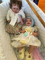 Two reborn dolls laying together in fabric basket with tags visible showing item count and brand Bebesol Pink Collection on paper.