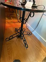 Side view of the round black marble top table with wrought iron scrollwork legs on a hardwood floor.