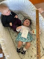 Two reborn sleeping dolls lying on a padded white surface with a measuring stick beside them.