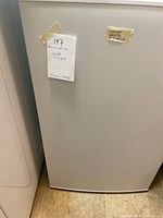 White small upright freezer with tape tags on the front.