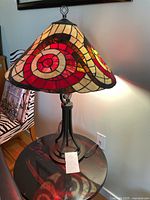Full view of stained glass lamp on black table showing the shade's vibrant geometric pattern and the metal base.
