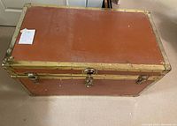 Front view of vintage cedar-lined blanket trunk showing reddish-brown exterior with brass-colored metal trim and central lock.