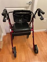 Front view of the burgundy metal frame walker with black padded seat and black backrest pouch.