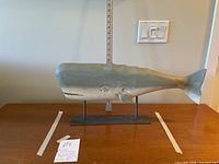 Side view of the whale sculpture with tape markers showing dimensions and a tag indicating lot number.