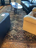 Photo showing overall view of the carpet placed under a table and between sofas, illustrating the full pattern and condition.
