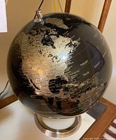 Black and gold world globe showing North America region, on metal stand.