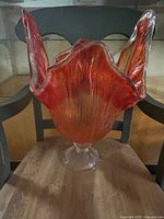 Front view of vintage red glass vase with petal-shaped flared edges on clear pedestal base, showing color and texture.