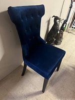 Front and side view of blue velvet accent chair with tufted backrest and black wooden legs.