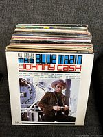 Photo of the front vinyl album cover of "All Aboard The Blue Train with Johnny Cash" featuring Johnny Cash in front of a train, showing part of the stacked vinyl records behind it.