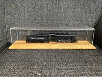 Full view of the miniature train set housed in a transparent display case on a wooden base.