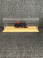Miniature model train inside clear display case on wooden base.