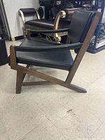 Side view of wooden lounge chair showing angular frame, black upholstery on seat and backrest, and signs of wear on legs.