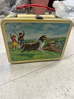Front view of the tin lunch box showing painted outdoor scene with collie dog, two children fishing, and rural background.