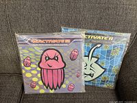 Photo showing the two sealed LP records Reactivate 11 and Reactivate 12 placed side by side on a sofa with their colorful animated designs visible.